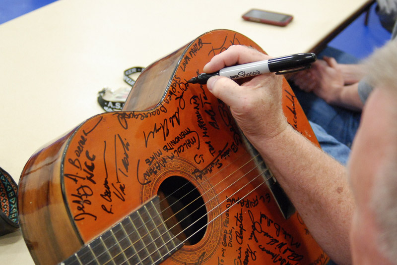 man adding signature to many already on a guitar